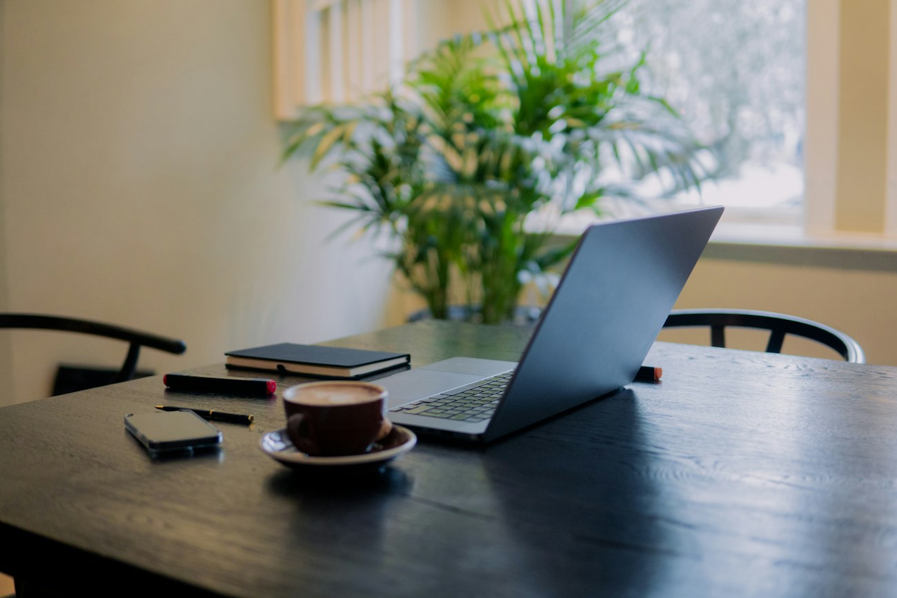 Sunlit professional workspace with laptop, notebook and coffee